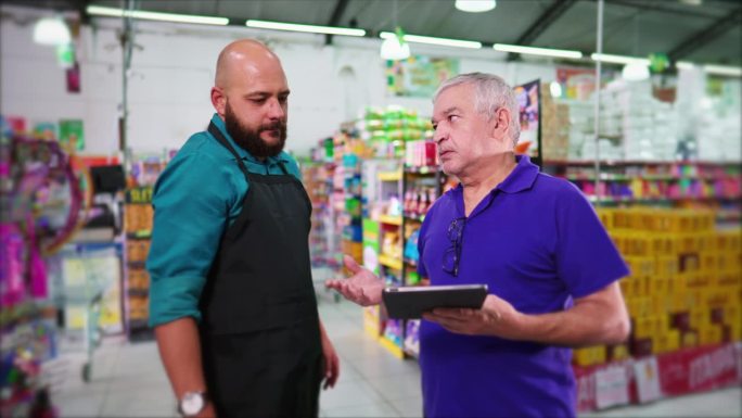 超市老年经理训斥员工，商业老板训斥杂货店拿着平板电脑的员工，显示库存不足