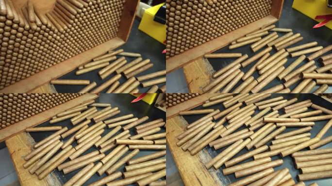 俯视图，许多刚刚卷过的没有标签的手工雪茄被堆放在一堆，随意散落在一张木桌上。这家工厂生产世界上最好的