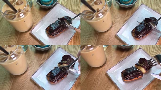 一块覆盖着黑巧克力的蛋奶蛋糕用刀叉切下来，旁边是一杯冰咖啡，盘子在木桌上动来动去，不方便切