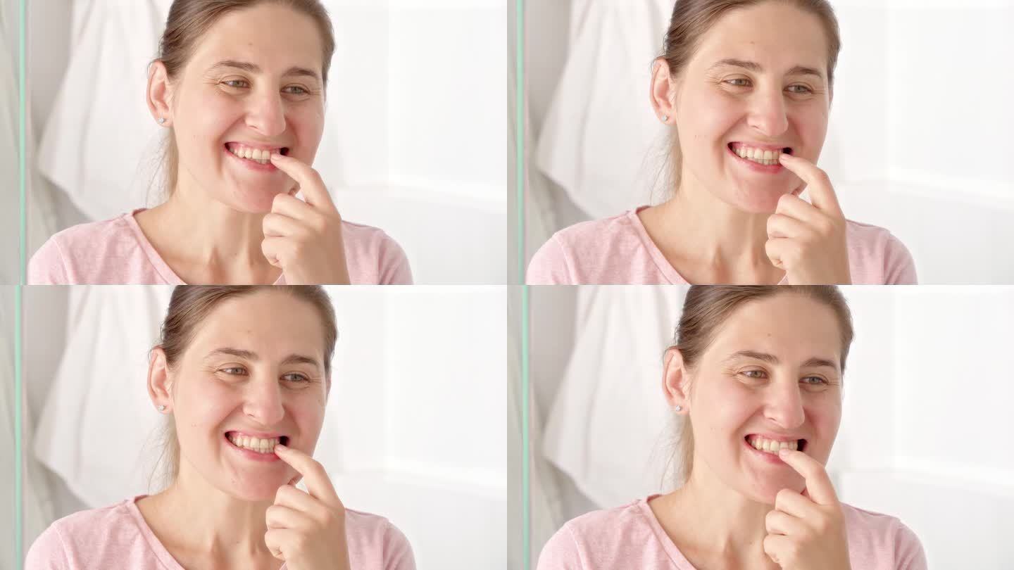 年轻女子在照镜子时用手指擦拭牙菌斑的特写。牙齿健康观念，自我检查口腔及口腔卫生