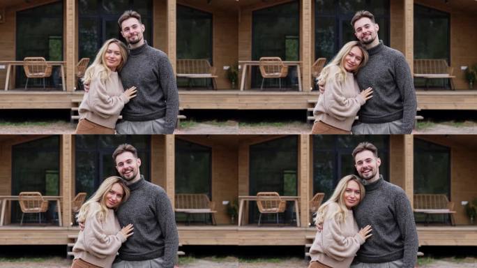 幸福的夫妇站在木制避暑别墅的院子里看着相机拥抱的肖像。正景中景白人帅哥美女周末休闲写真。