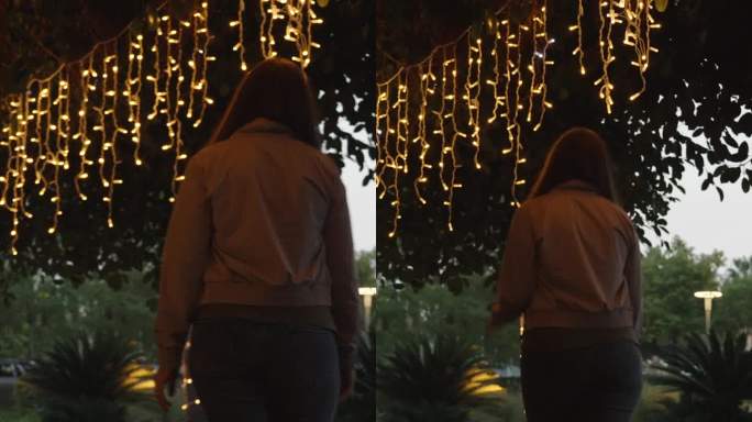 垂直视频。一位年轻女子带着新年花环走在树下，棕榈树上缠着灯笼。