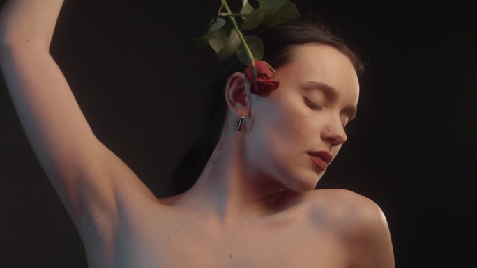 性感的女人用红色的口红和纹身黑色背景工作室拍摄跳舞与一个单一的红玫瑰和感觉花瓣对皮肤
