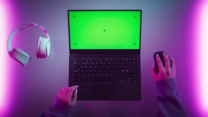 一个女性软件开发人员在一个有霓虹灯的时髦房间里用笔记本电脑工作的自上而下的照片。电脑与绿色屏幕色度键