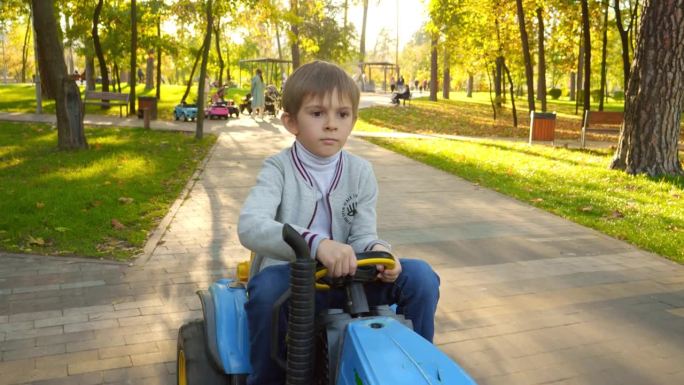 在秋天的公园里，小男孩开着儿童拖拉机。孩子们在公园里玩耍，种地，开车。