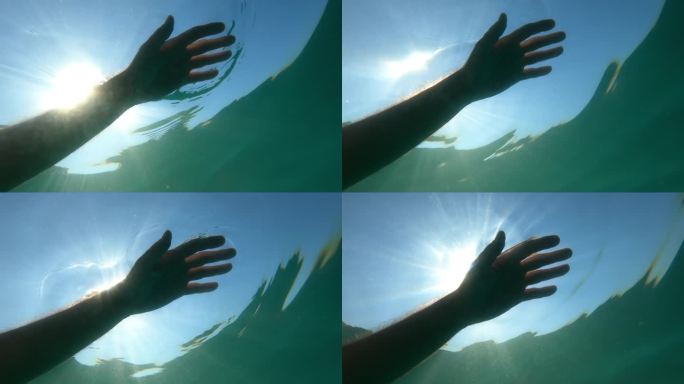 一名溺水者的手漂浮在海水中，背部被夏日炎热的阳光照亮，水下拍摄低角度视角