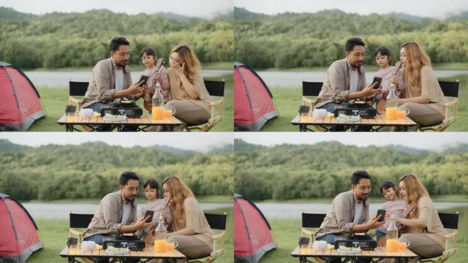 亚洲父母和女儿在阳光明媚的湖边露营地的帐篷里用照相手机自拍。