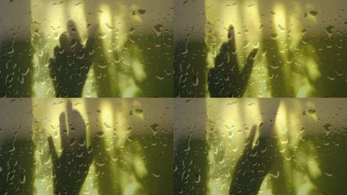 模糊的阴影女性的手在黄色的墙壁背景，透过潮湿的玻璃窗与雨滴。舞蹈和放松，光和影，大气的秋天心情和健康