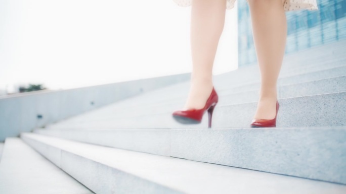 一个不知名的女人穿着裙子和红色细高跟鞋走下一座现代建筑前的楼梯
