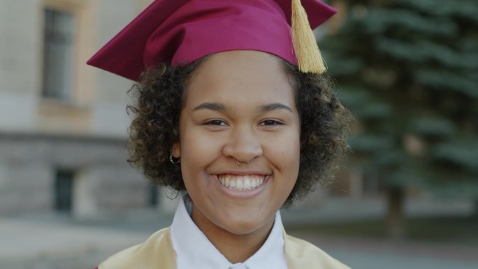 大学门前，骄傲的非裔美国女士戴着毕业帽在户外微笑的特写