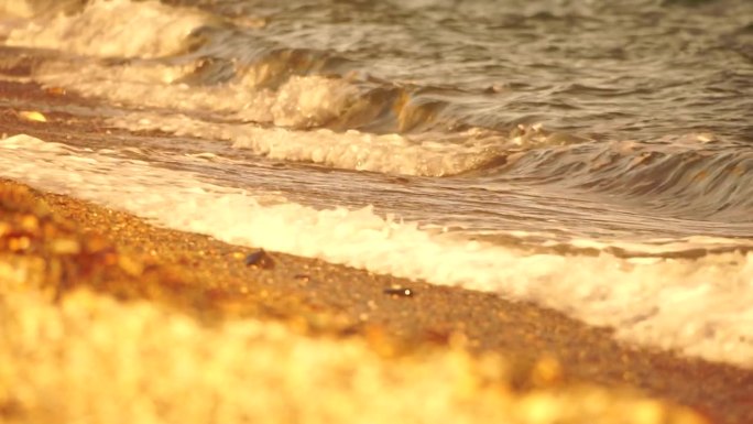 小海浪，模糊的软泡沫海浪冲刷金色卵石沙滩夕阳。海滩上的海浪。没有人。假日休闲概念。抽象航海夏季海洋日