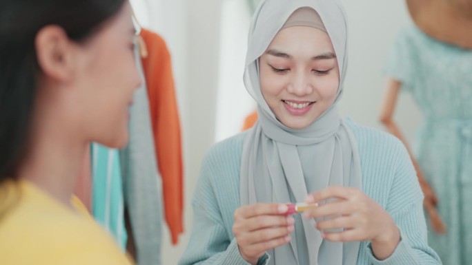 一名戴着头巾的穆斯林年轻成年妇女正在给她的顾客用唇色化妆品化妆。