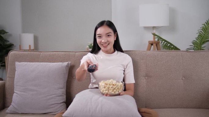 亚洲年轻漂亮的女人在家里看有趣的电视电影。有吸引力的休闲女孩感到快乐和放松。