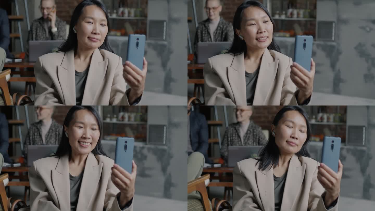 雄心勃勃的亚洲女商人用智能手机和耳机进行在线视频通话，在办公室里挥手致意