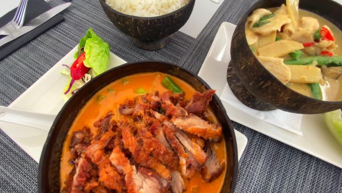 传统泰式红咖喱脆皮鸭和绿咖喱鸡配米饭在椰子碗，泰式餐厅，4K顶级镜头