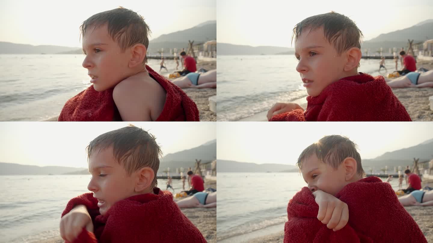 小男孩在海里游泳后裹着红毛巾感到冷的照片。假期、暑假、旅游。