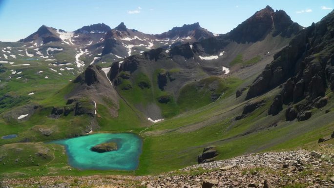 航拍电影俯瞰冰湖盆地西尔弗顿岛湖水蓝色清澈的水高山苔原令人惊叹的山脉雪野花仲夏白天美丽的慢盘向左移动
