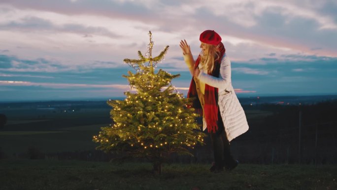 黄昏时分，一名妇女打开户外圣诞树上的串灯