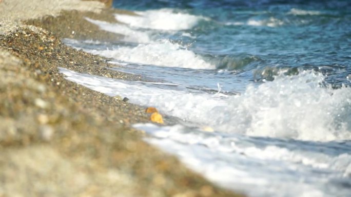 小海浪，模糊的软泡沫海浪冲刷金色卵石沙滩夕阳。海滩上的海浪。没有人。假日休闲概念。抽象航海夏季海洋日