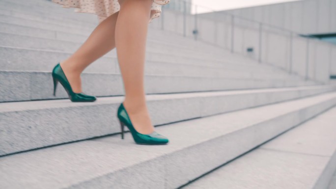 一个不知名的女人穿着裙子和翡翠绿的细高跟鞋走下城市的楼梯