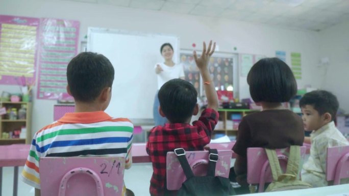 一群学校的亚洲孩子坐在教室里，举起手臂回答老师的问题。回归学校和教育理念。慢镜头。