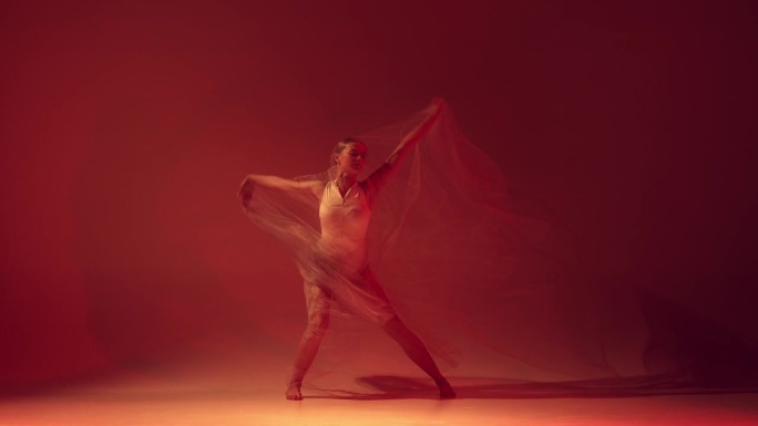 吸引力和性感。年轻的女孩，专业的芭蕾舞演员，在霓虹灯的红色工作室背景下，用透明的织物跳舞