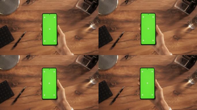 一个人拿着智能手机的自上而下的视图，模拟绿色屏幕Chromakey显示与运动跟踪占位符。木制办公桌与
