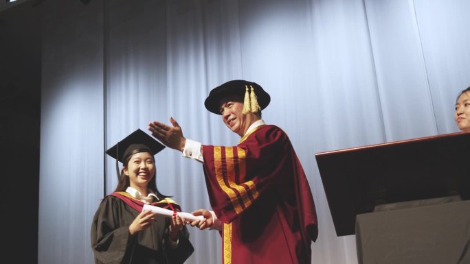 毕业典礼激动的亚洲毕业大学女学生在礼堂的舞台上接过毕业奖状后，举起手臂站在院长身边