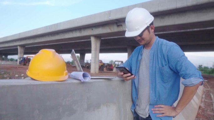 图为，亚洲的土木工程师正在用笔记本电脑和设计图检查在施工现场进行的高速公路工程。