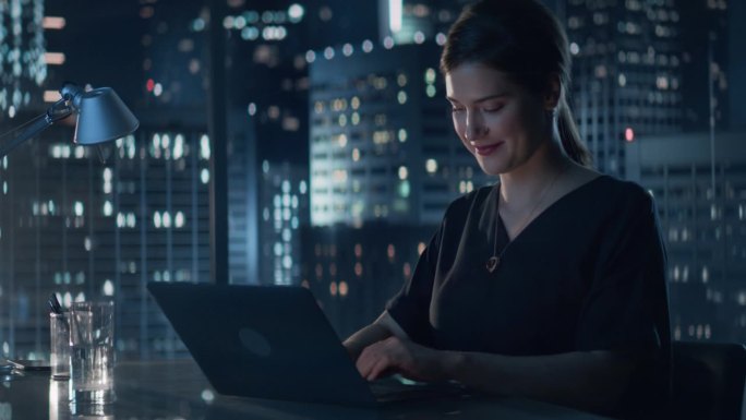 年轻成功的白人女商人深夜坐在办公桌旁用笔记本电脑工作的画像。女性金融分析师进行股票市场研究。