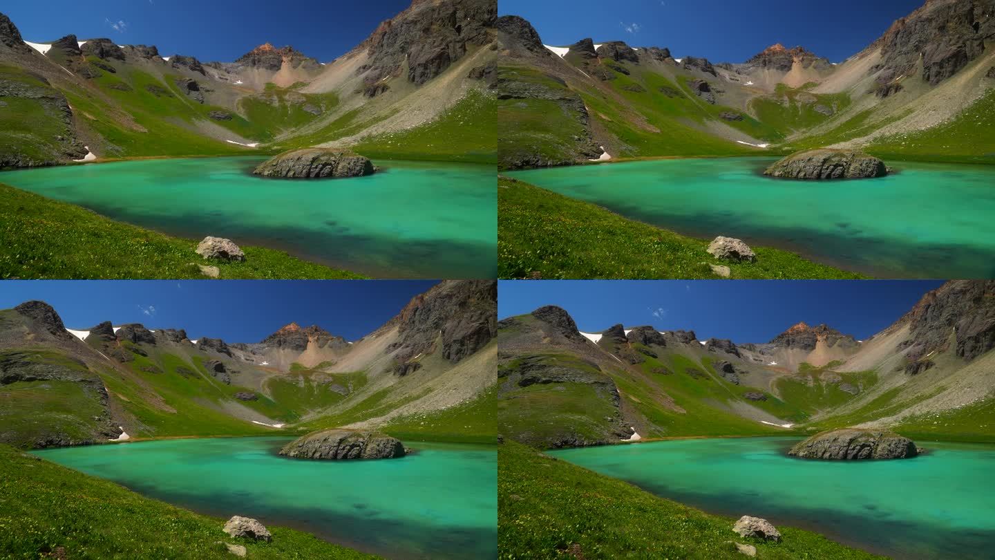 航拍电影无人机冰湖盆地西尔弗顿岛湖夏季水蓝色清澈的水高山苔原令人惊叹的山脉雪野花白天美丽缓慢的锅向左