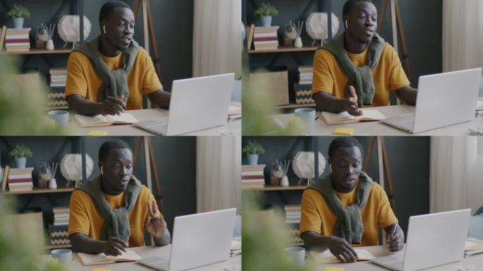 非裔美国人自由职业者，使用笔记本电脑和无线耳机在笔记本上进行视频通话和写作