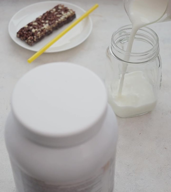 男手将牛奶倒入玻璃罐中，制作乳清蛋白饮料冰沙的过程，运动营养，垂直视频