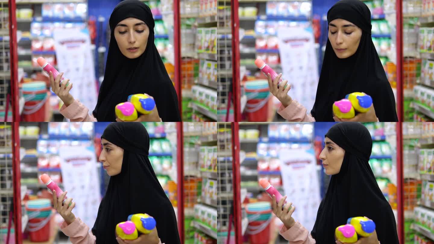 一位戴着头巾的穆斯林妇女站在那里，手里拿着三种化妆品，比较它们的成分和价格。一位精心打扮的伊斯兰妇女