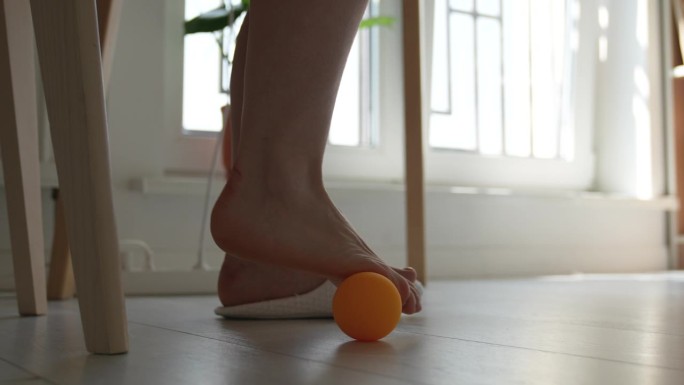 女性在长时间久坐不动的工作中使用硅胶球在桌下进行足部按摩。