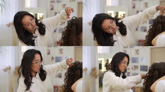 在现代美容工作室里，专注的女发型师在使用定型剂后用梳子和手把长而卷曲的头发定型。