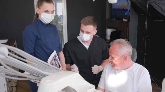 一位老人坐在牙科椅上听牙医讲话。为退休人员种植牙齿