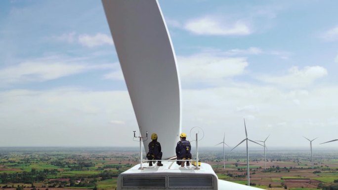 男女检查工程师坐在风力涡轮机的顶部，看着美丽的风景