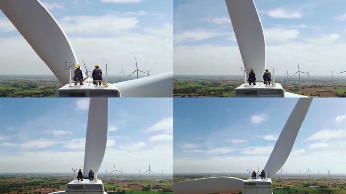 男女检查工程师坐在风力涡轮机的顶部，看着美丽的风景