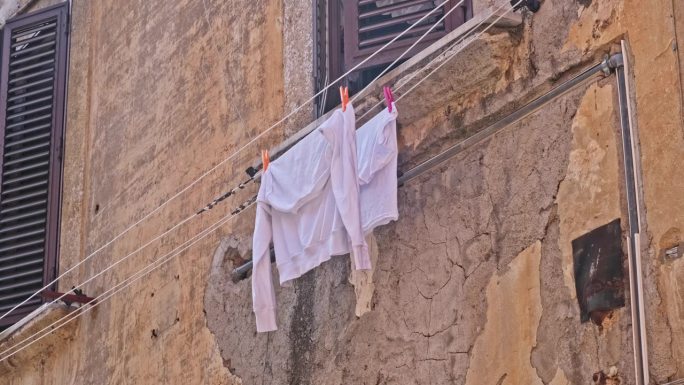 在意大利老城的一条街上，湿的白色棉质运动衫晾在晾衣绳上