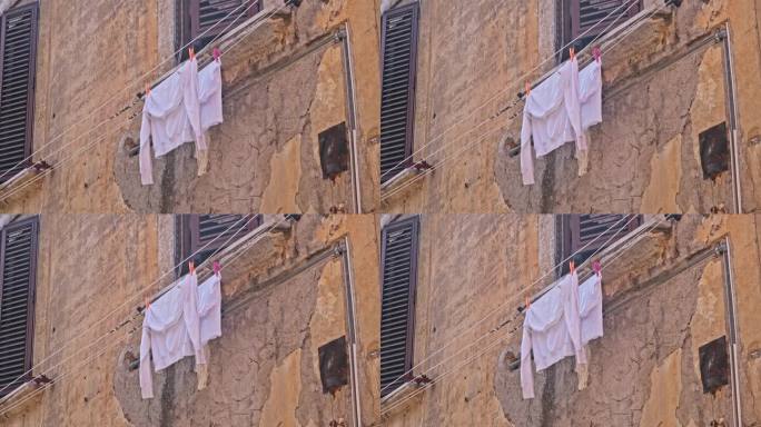 在意大利老城的一条街上，湿的白色棉质运动衫晾在晾衣绳上