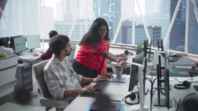 在一家现代公司里，两位年轻的印度财务顾问在电脑旁讨论股市策略。南亚经理在银行研发中心工作