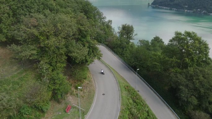 无人机拍摄的男子骑着摩托车在铺砌的道路上穿过大自然