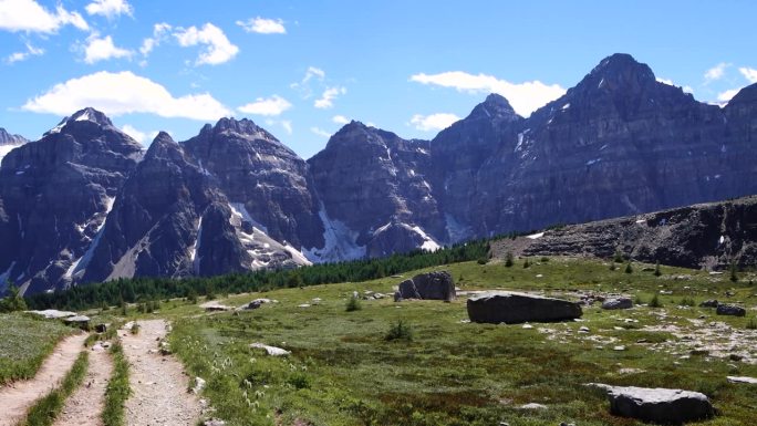 背着红色背包的徒步旅行者在通往哨兵山口的小路上，可以看到十个山峰的山谷和落叶松山谷茂密的松树林。加拿
