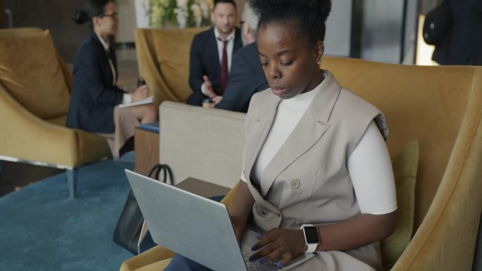 一位雄心勃勃的非裔美国女商人坐在酒店休息室用笔记本电脑打字