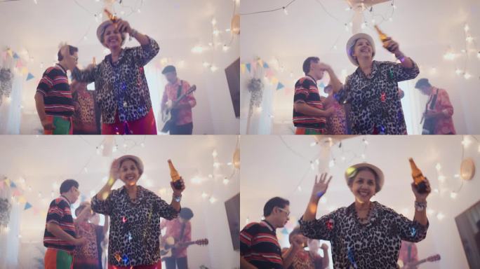 微笑的老年妇女端着啤酒庆祝新年，朋友们在家里唱歌跳舞。