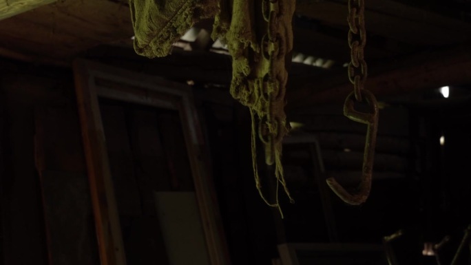 生锈的铁链从天花板上垂下来，在一个废弃的地下室里晃来晃去，一条金属链和生锈的钩子在一个旧谷仓里移动