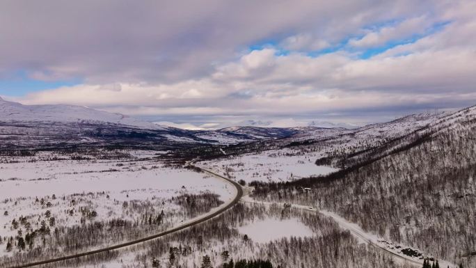 挪威冬季自驾游，航拍森林中风景优美的公路，景观被雪覆盖，白云满天。