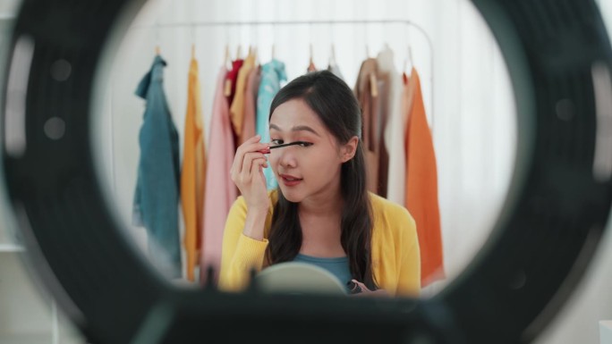 一名亚洲年轻成年女子在社交媒体上直播时，用睫毛刷在脸上给粉丝们看。