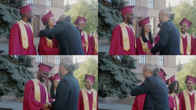 骄傲的教授在大学外祝贺戴着毕业帽、穿着毕业服的不同群体的学生，他们握手拥抱